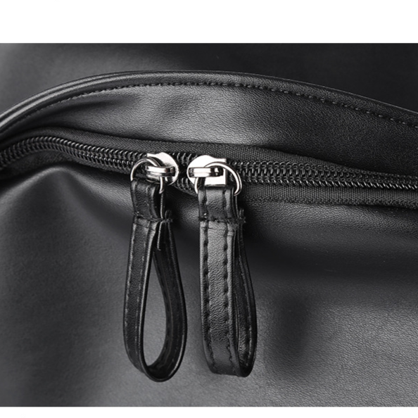 Close-up of a black leather bag with zipper pulls on a dark background